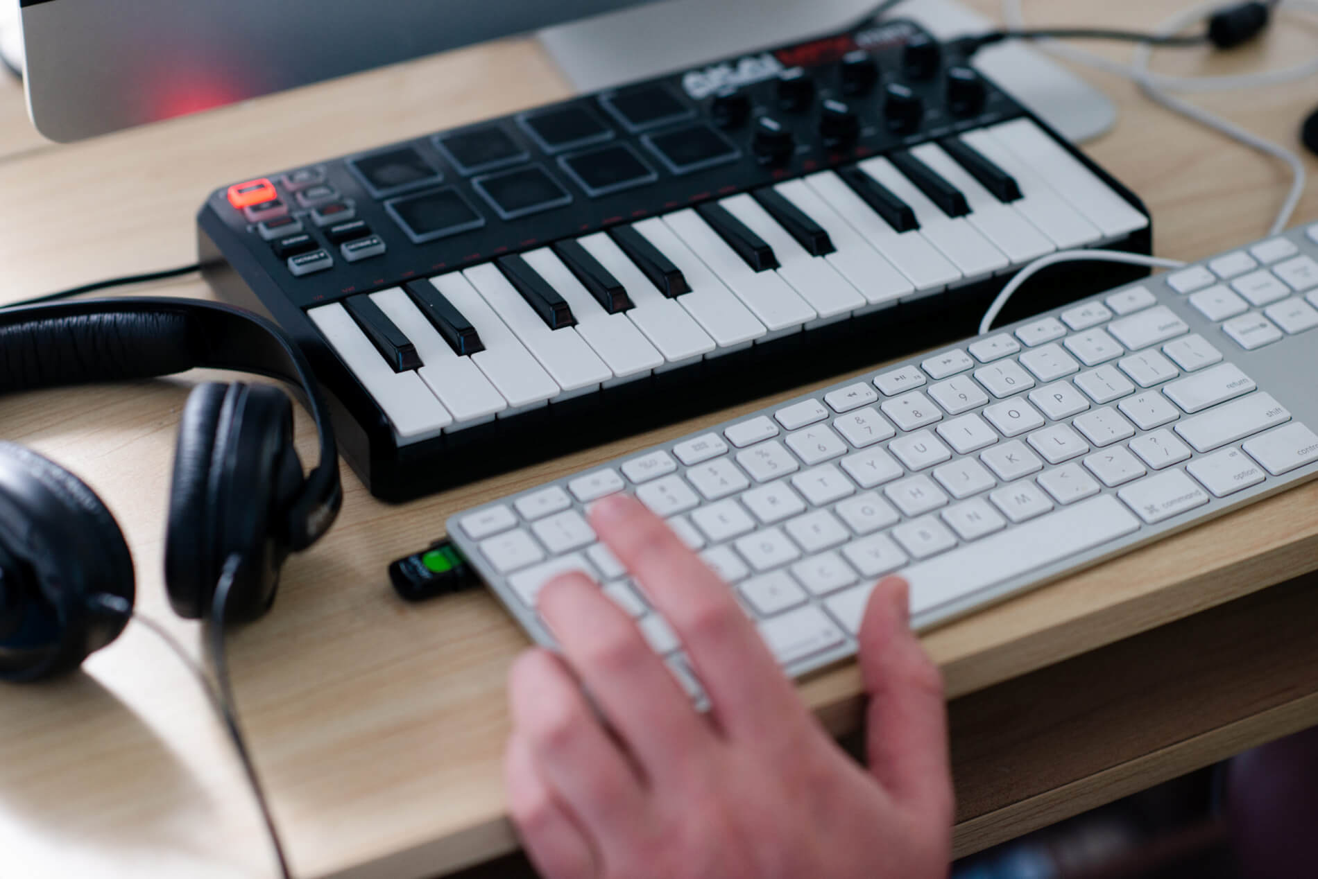 Image of audio keyboard, computer keyboard and headphones on desk. Hand hovers over QWERTY keyboard.