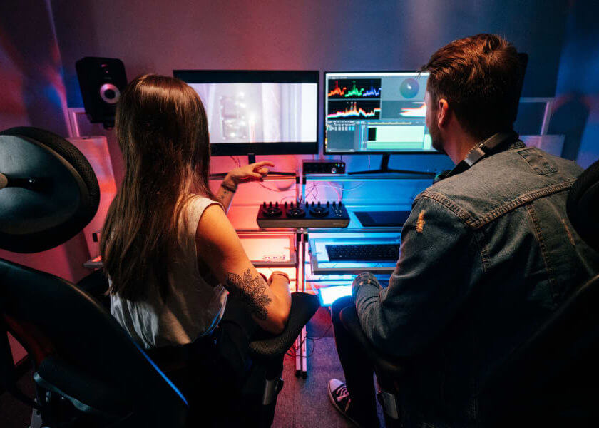 Two people sit in chairs facing computer monitors with software on it