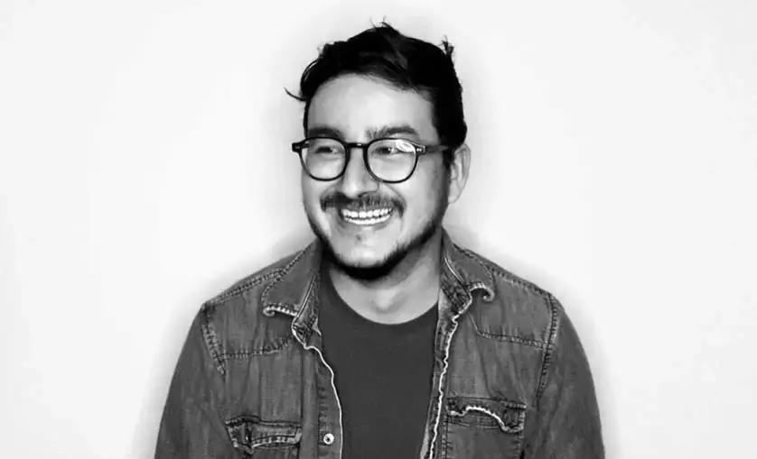 Portrait image of man wearing optical glasses smiling and looking off into the distance. SAE graduate Aldo Arechar