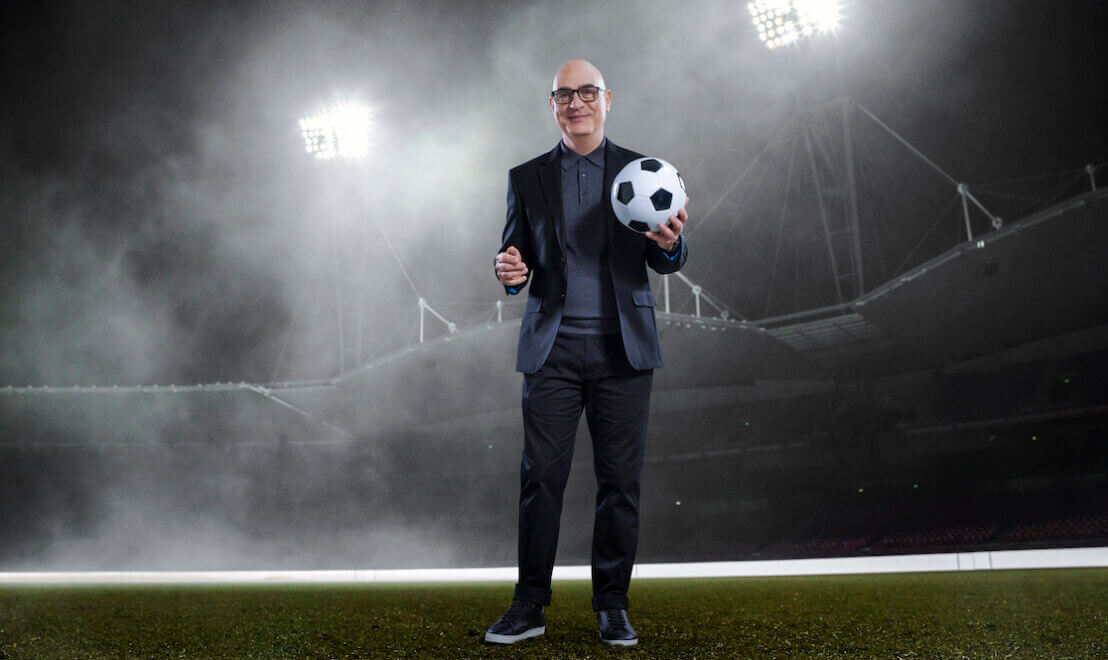 Man in a suit holding a football in an empty stadium at night