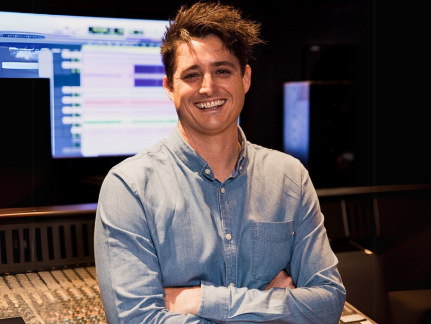 man smiles with crossed arms in front of studio backdrop